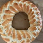 A round, braided loaf of bread with a golden-brown crust on a parchment-lined surface.