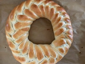 A round, braided loaf of bread with a golden-brown crust on a parchment-lined surface.