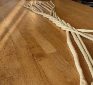 Twisted ropes of white dough are laid out on a wooden surface, partially overlapping each other in a loose braid pattern.
