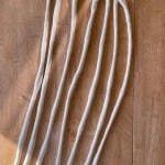 Seven elongated pieces of dough resting on a wooden surface.