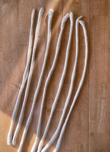 Seven elongated pieces of dough resting on a wooden surface.