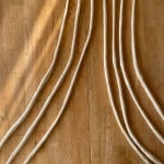 Unbaked dough rods are neatly arranged on a wooden table, illuminated by sunlight.