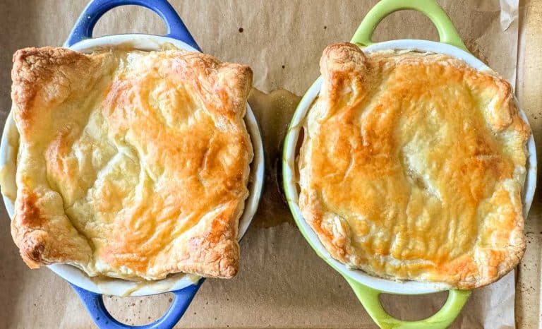 Two baked pot pies in blue and green handled dishes on parchment paper, with golden brown crusts.
