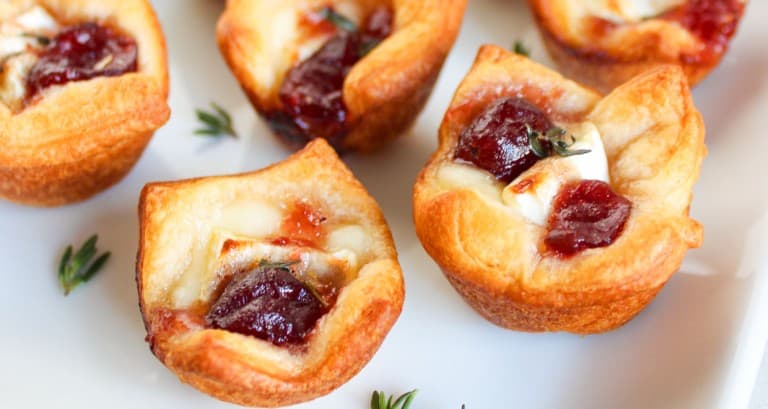 Mini pastry cups, perfect appetizers, filled with cheese and jam, garnished with herbs, served on a white plate.