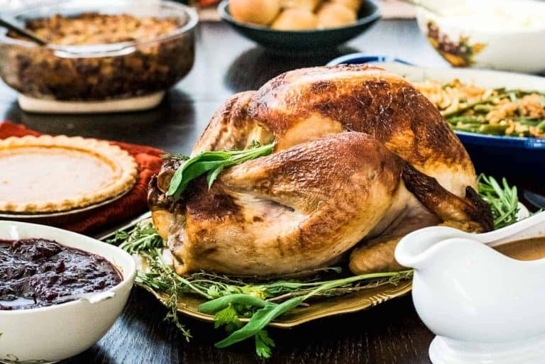 Roasted turkey takes center stage on a platter with herbs, surrounded by delightful dishes like pie, cranberry sauce, green beans, and gravy—all showcasing the essence of classic turkey recipes on a festive dining table.