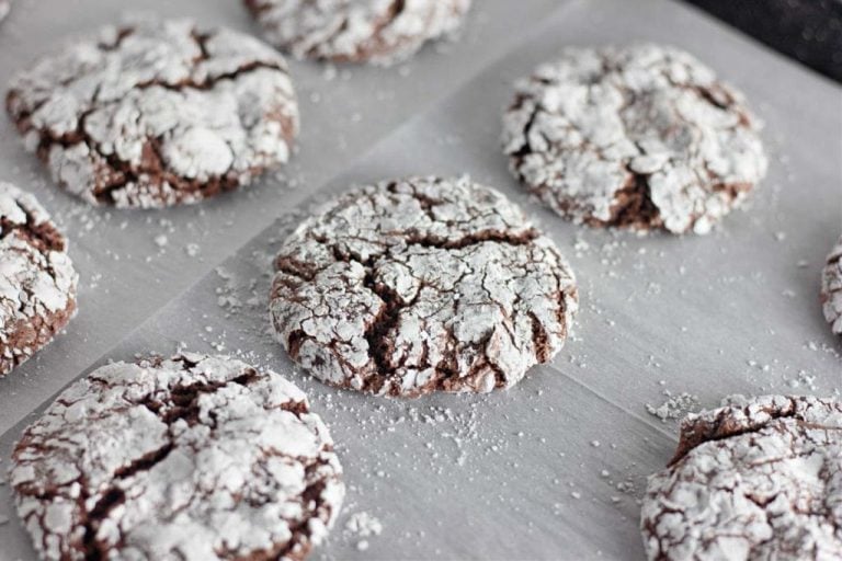 Chocolate crinkle cookies dusted with powdered sugar on parchment paper.