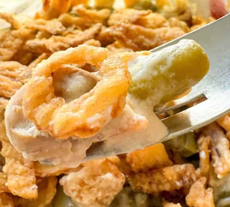 A fork holding a bite of green bean casserole topped with creamy sauce and crispy fried onions.