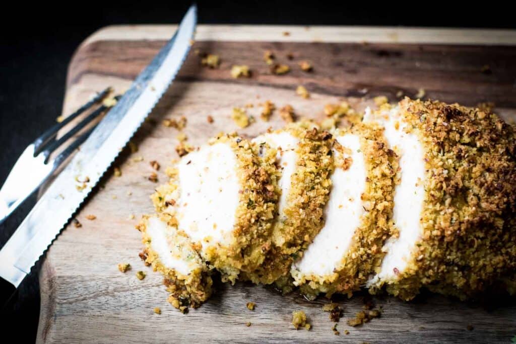Sliced breaded chicken resembles a classic turkey recipe arrangement on a wooden cutting board next to a knife.