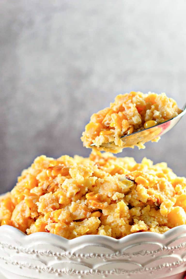 A bowl of cornbread casserole with corn, topped with a golden crust. A spoon holds a portion above the bowl.