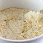 A bowl of corn casserole mixture being stirred with a wooden spoon.