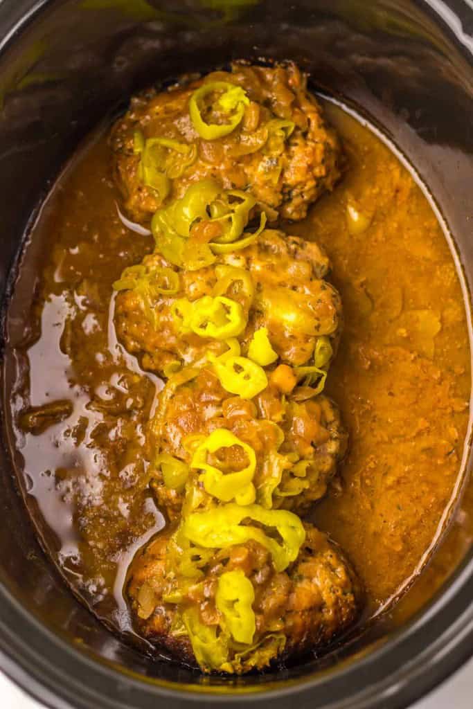 Plate of meatloaf with mashed potatoes, peas, and carrots on a blue cloth. A wooden spoon and drink are in the background.