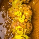 Meatballs covered in sauce and topped with sliced peppers in a slow cooker.