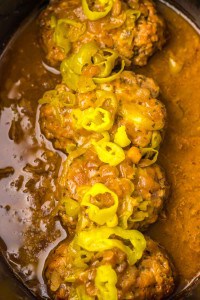 Meatballs covered in sauce and topped with sliced peppers in a slow cooker.
