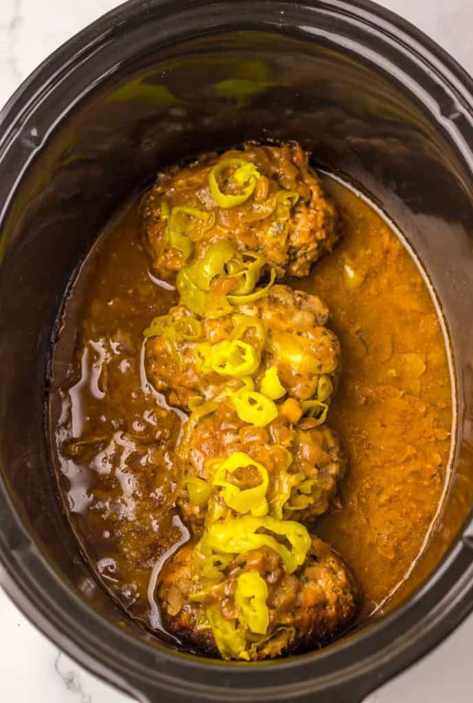 Slow cooker with cooked meat and sliced yellow peppers in a sauce.