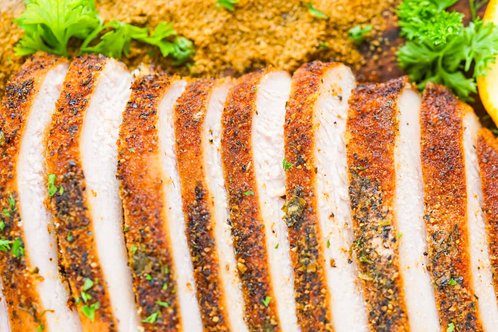 Grilled chicken breast, expertly sliced and seasoned, is garnished with fresh parsley and a lemon wedge, displayed elegantly on a wooden board—perfect for those exploring new turkey recipes.