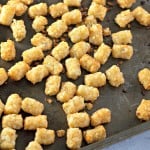 Golden tater tots scattered on a baking sheet.