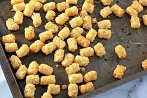 Golden tater tots scattered on a baking sheet.