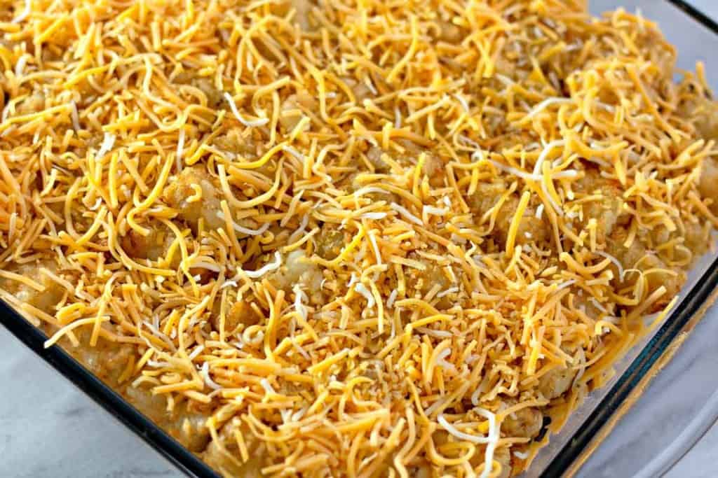 A glass baking dish filled with cheesy enchiladas ready to be baked.