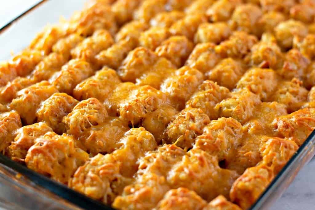 A glass baking dish filled with a golden-brown tater tot casserole, topped with melted cheese.