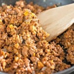 Cooked ground beef with onions in a skillet, being stirred with a wooden spatula.