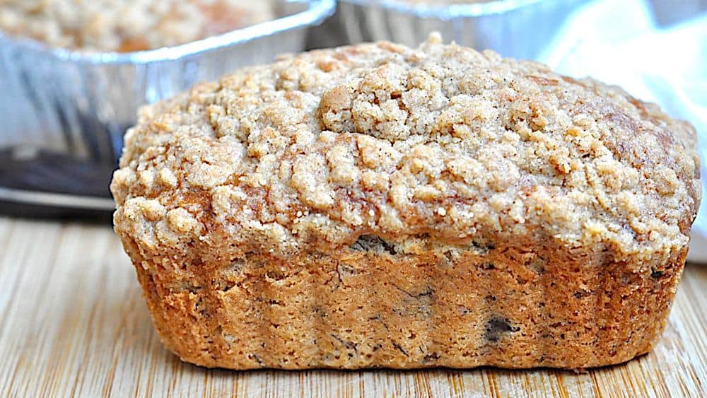 A loaf of banana bread with a crumbly topping, resting on a wooden surface.