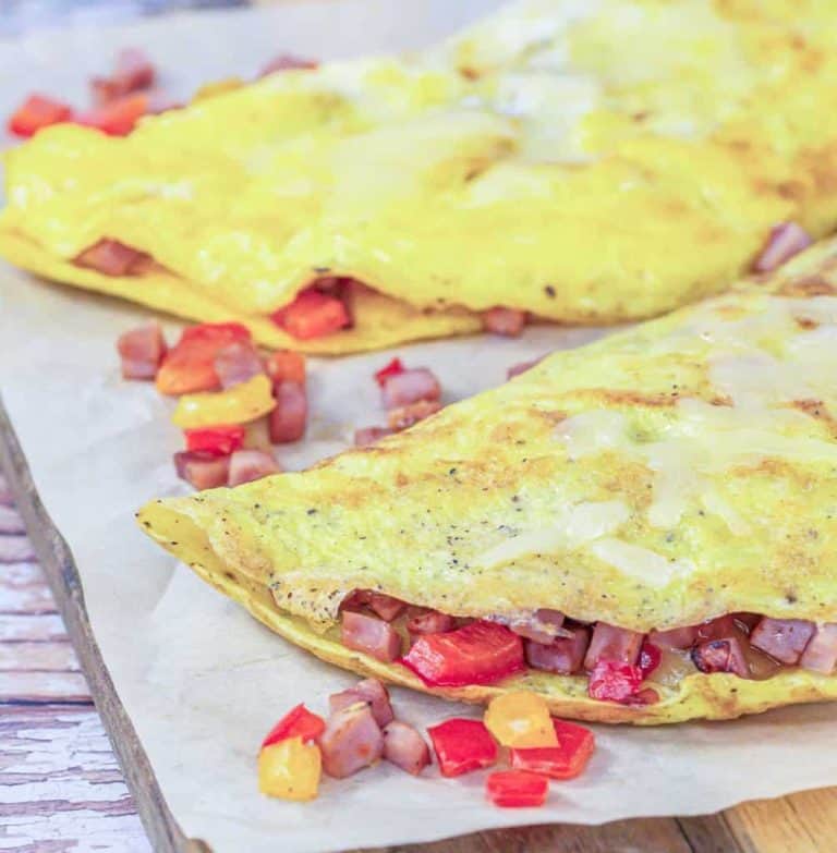 Two omelettes filled with diced ham and red and yellow bell peppers, placed on parchment paper.