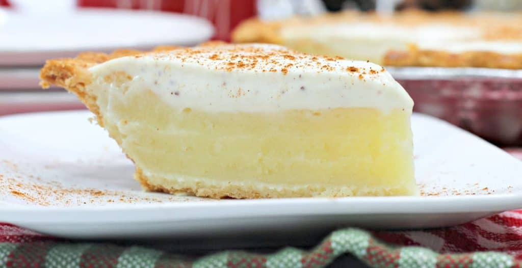 A slice of cream pie on a white plate, topped with whipped cream and a sprinkle of cinnamon.