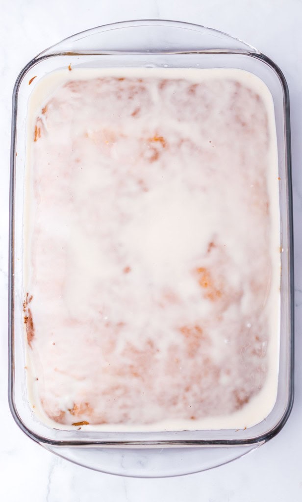 A large rectangular cake with white icing in a clear glass baking dish on a marble surface.