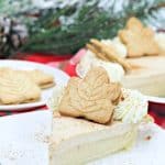Slice of a pie garnished with leaf-shaped cookies and whipped cream on a plate, with a festive background.