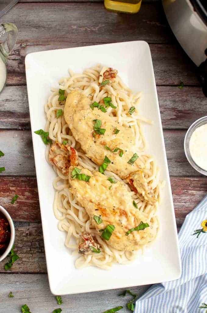 A rectangular plate of creamy chicken served on a bed of pasta, garnished with chopped herbs.