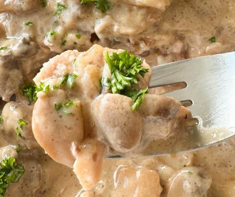 Close-up of a fork holding chicken pieces in creamy sauce with mushrooms, garnished with parsley.