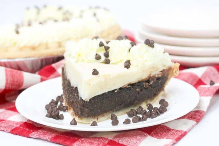 A slice of chocolate pie with cream topping and chocolate chips on a white plate, set on a red and white checkered cloth.