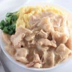 A plate with chicken and dumplings in gravy, served with mashed potatoes and a garnish of cilantro. A fork is placed beside the plate.