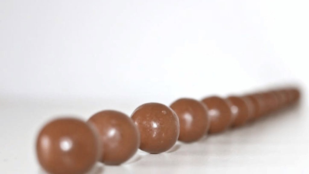 A row of brown spherical chocolate candies arranged in a line on a white surface, with a blurred background.