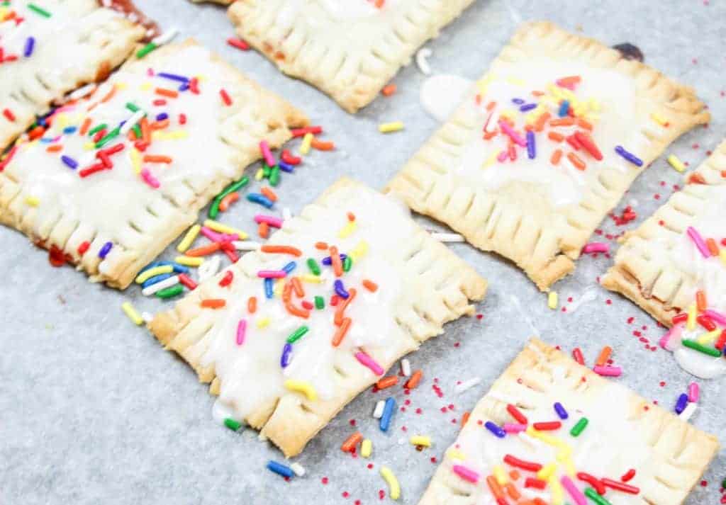 Pastries with white icing and colorful sprinkles arranged on a baking sheet lined with parchment paper.