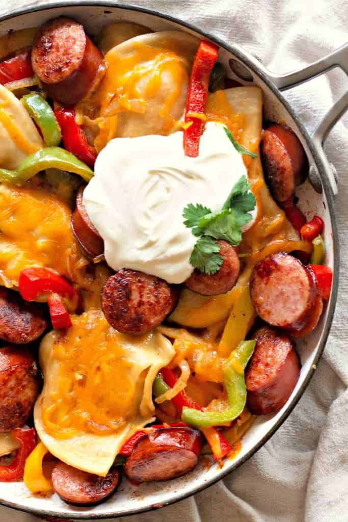 A Pierogi and Kielbasa Skillet brimming with cooked sausage slices, vibrant bell peppers, tender pierogi, melted cheese, and finished with a dollop of sour cream and fresh cilantro.