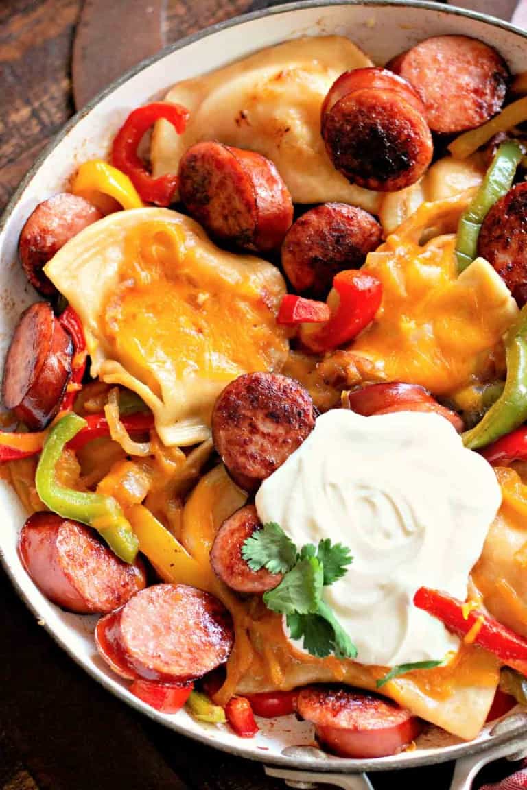 A Pierogi and Kielbasa Skillet bursts with flavor, featuring pierogies, sliced sausage, bell peppers, onions, melted cheese, and a dollop of sour cream garnished with cilantro.