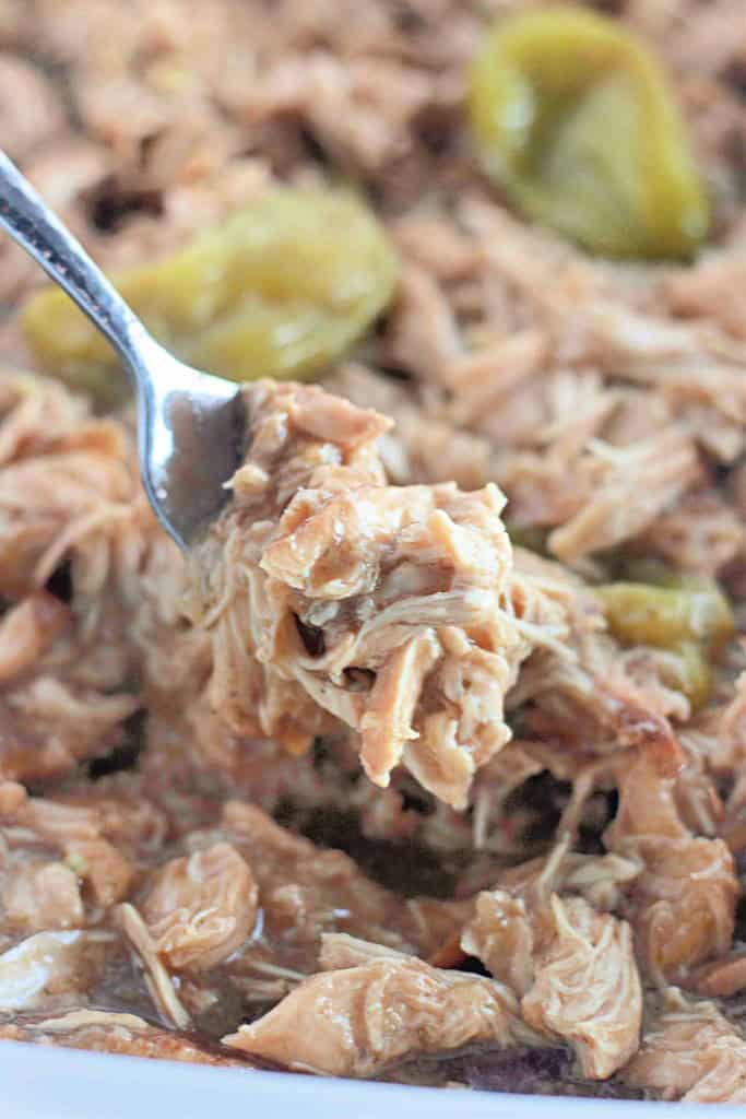 Close-up of a fork holding shredded chicken with jalape&ntilde;o slices in the background.
