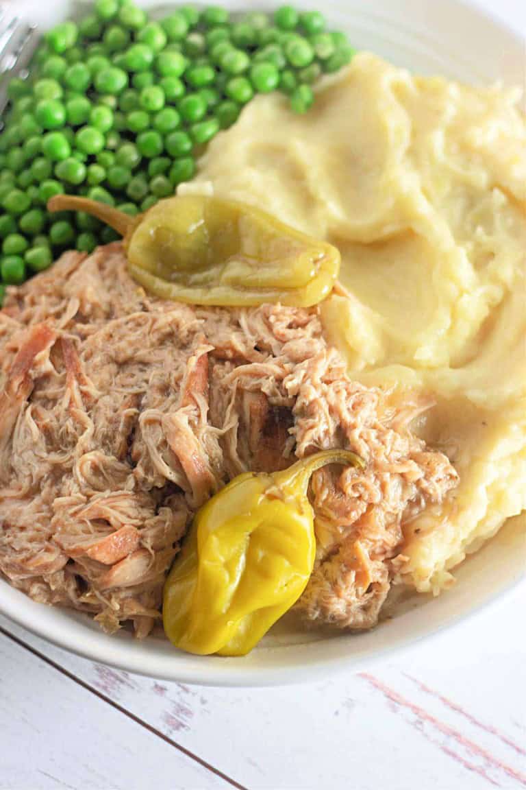 A plate with shredded chicken topped with peppers, mashed potatoes, and green peas.