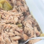 Shredded cooked meat with sliced green peppers in sauce, served in a white dish with a metal spoon.