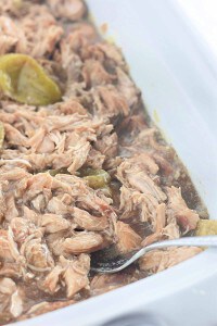 Shredded cooked meat with sliced green peppers in sauce, served in a white dish with a metal spoon.