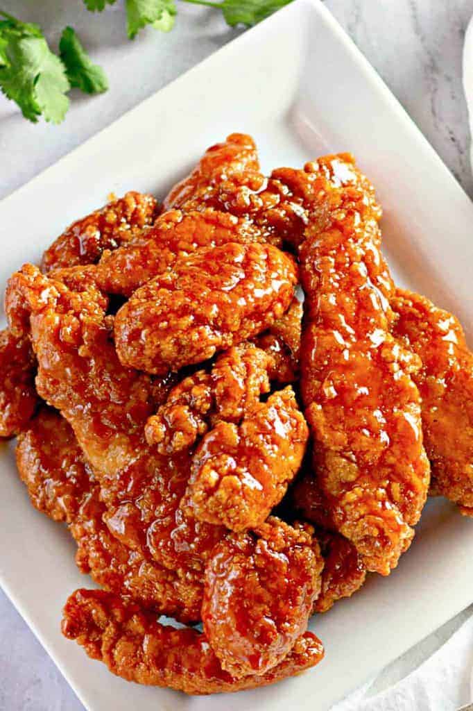 Plate of crispy fried chicken tenders coated in a glossy, golden-brown sauce on a white square dish.
