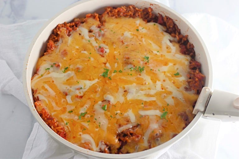 A skillet filled with a flavorful taco rice dish, topped with melted cheese and garnished with fresh parsley.