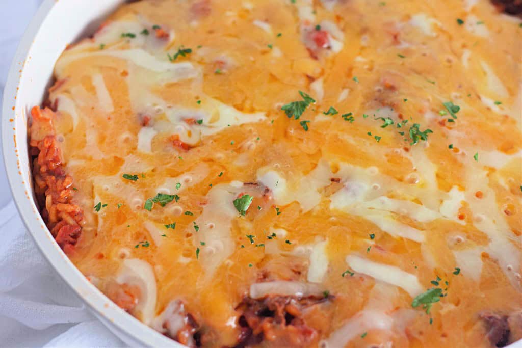 A baked taco rice skillet, covered in melted cheese and sprinkled with chopped parsley on top, reveals hints of rice and tomato underneath.