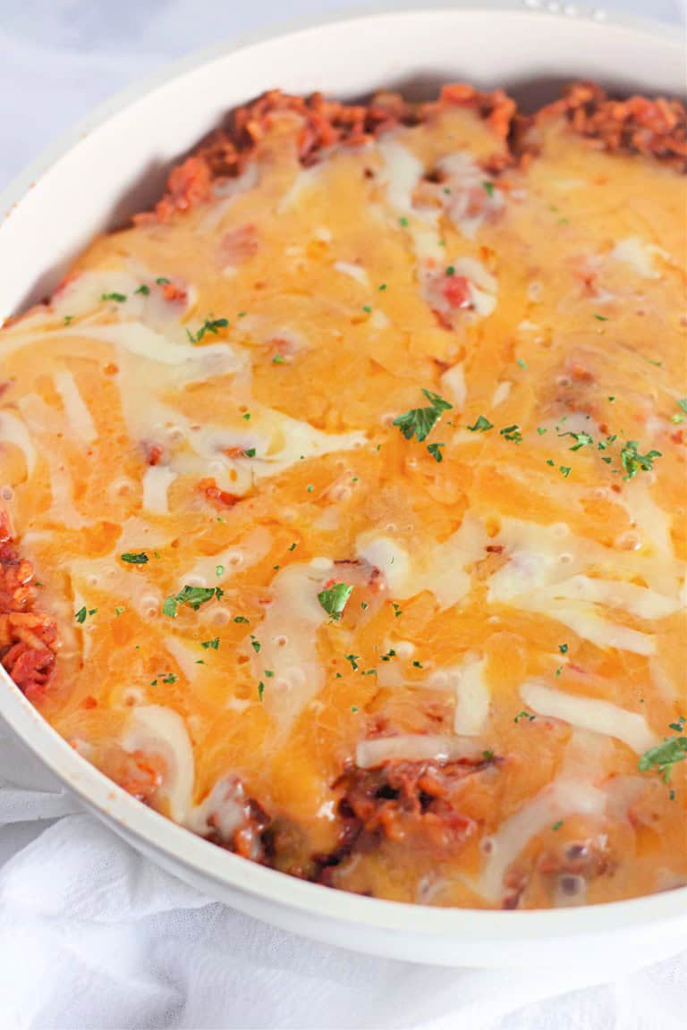 Baked cheesy taco rice casserole dish with a golden top, sprinkled with chopped parsley, in a white oval baking dish.