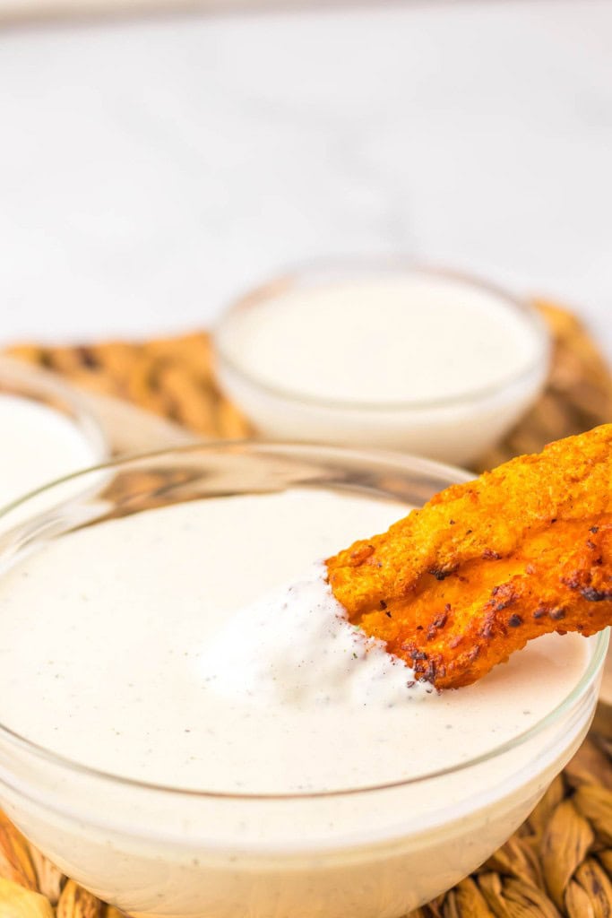 A fried plantain dipped in creamy sauce, served in a clear bowl.