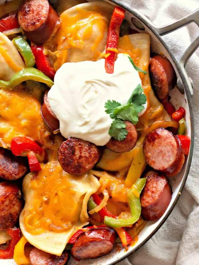 Pan of pierogies with smoked sausage, bell peppers, melted cheese, and a dollop of sour cream topped with cilantro.