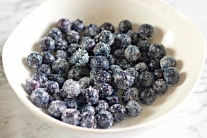 A white bowl filled with frosted blueberries sits on a marble surface, reminiscent of the sweet allure found in Blueberry Danishes.