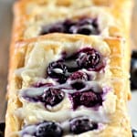 A row of blueberry Danishes topped with fresh blueberries and drizzled with icing.