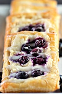 A row of blueberry Danishes topped with fresh blueberries and drizzled with icing.
